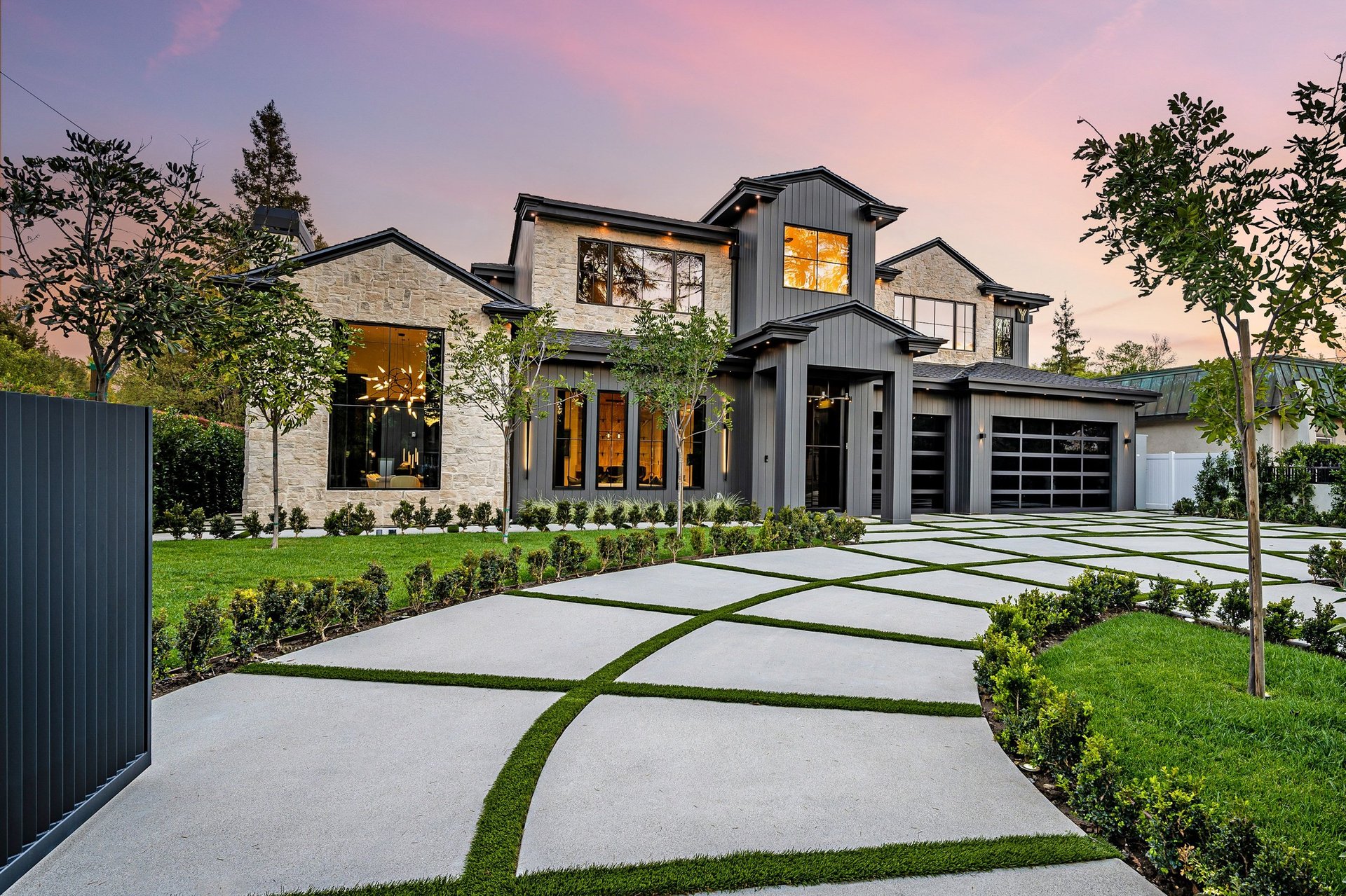 Modern luxury home exterior with a well-manicured lawn, geometric driveway, and sunset sky in the background